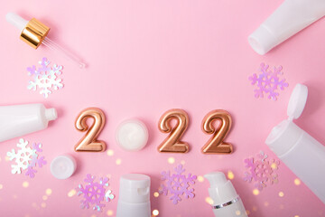 Obraz na płótnie Canvas Top view of the cosmetics containers on pink background.Rose gold numbers 2022 and festive bokeh above.Good for new year offer and text overlay.