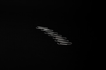 Fototapeta na wymiar Metal paper clips lie on a black background