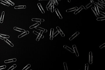 Metal paper clips lie on a black background