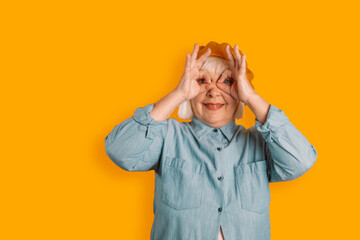 Friendly 40s 50s caucasian woman and stylish clothes having fun making glasses shape with hands isolated over bright orange color background