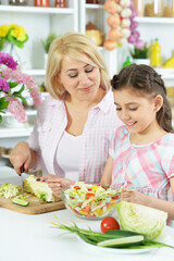 Cute little girl with her mother cooking together at kitchen table
