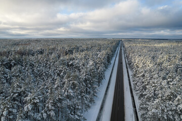 Aerial view of asphalt highway leading through frosty winter forests and groves covered with hoarfrost and snow. Drone photo of black road line and trees with chill snow in mountains. Christmas theme