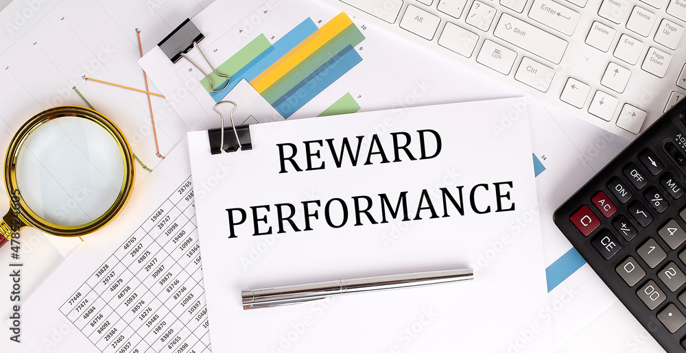 Poster reward performance text on the white paper on the light background with charts paper ,keyboard and c