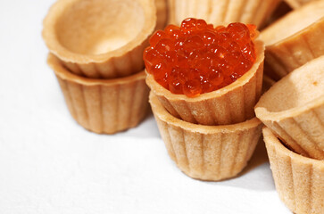Close-up of homemade tartlets baskets of puff pastry with red caviar, isolated on a white background.