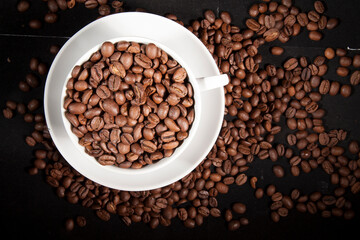 Cup of aromatic coffee with coffee beans on a dark background