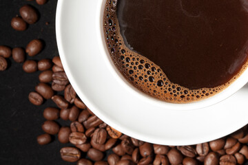 Cup of aromatic coffee with coffee beans on a dark background