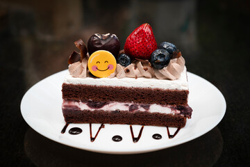 Piece of chocolate cake homemade with strawberry, blueberry and white cream toppings on a white plate and dark table background.