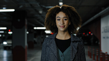 Beautiful young curly-haired african american girl millennial successful stylish woman female lady walking in parking lot of business shopping center looking at camera moving stepping inside indoors © Yuliia