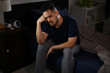 Fototapeta na wymiar Depressed young Asian man sitting in bed cannot sleep from insomnia