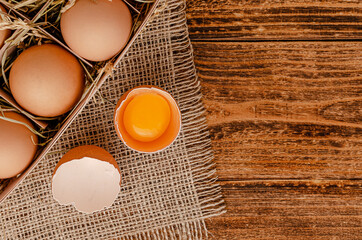 Brown eggs and broken egg with yolk on wooden background. Directly above, copy space.