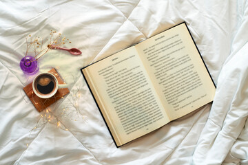 Open book and cup of coffee in bed