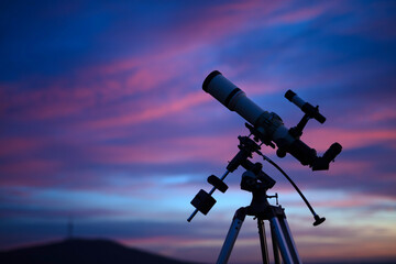 Silhouette of a telescope with colorful skies.