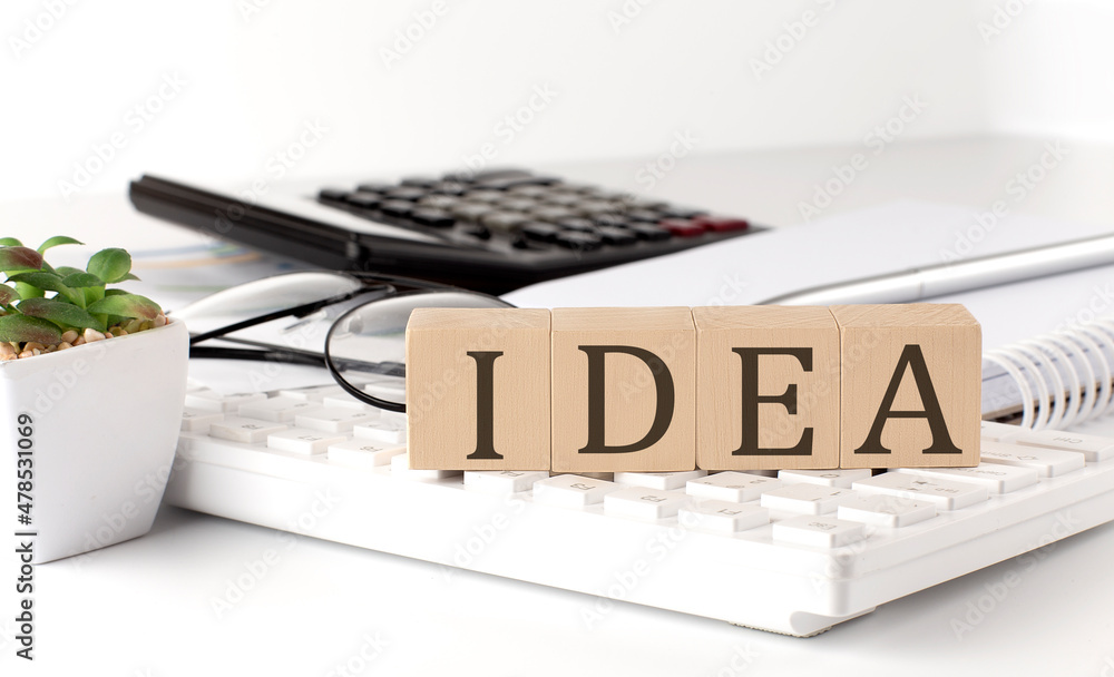Poster idea written on a wooden cube on keyboard with office tools