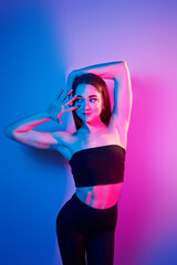 In black clothes. Fashionable young woman standing in the studio with neon light
