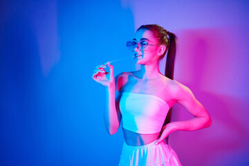 With chewing gum. Fashionable young woman standing in the studio with neon light