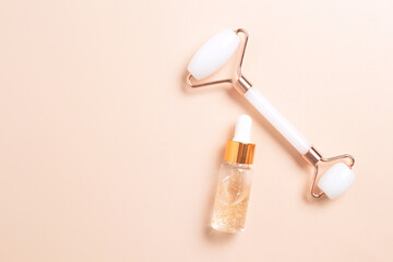 Bottle with dropper of aroma essential oil. Face roller on beige background. Creative trendy cosmetics flat lay with copy space