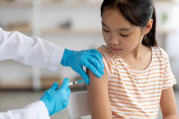 Unrecognizable doctor making vaccination for asian girl