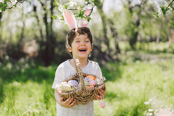 Easter egg hunt in spring garden. Funny boy with eggs basket and bunny ears on Easter egg hunt in...