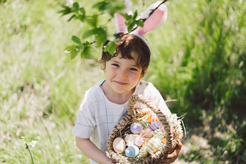 Easter egg hunt in spring garden. Funny boy with eggs basket and bunny ears on Easter egg hunt in...