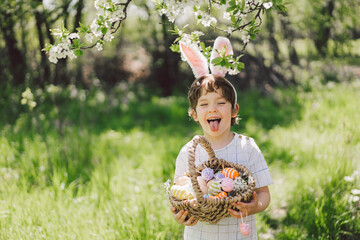 Easter egg hunt in spring garden. Funny boy with eggs basket and bunny ears on Easter egg hunt in sunny spring garden. Children celebrating Easter. Happy easter card