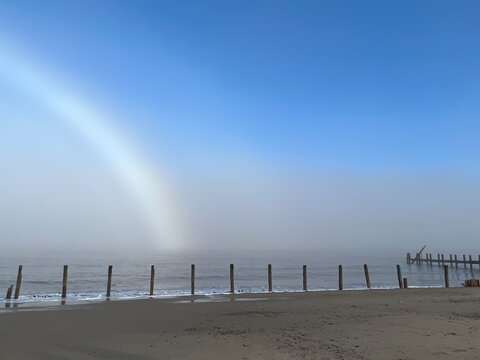 Beautiful beach landscape tranquil scene with fogbow over sandy shore by ocean at Happisburgh in Norfolk coast in East Anglia uk with blue skies after foggy mist cold morning in December