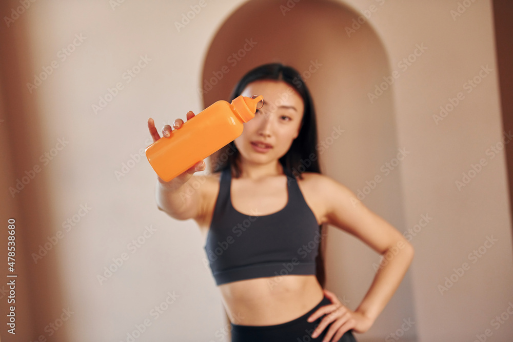 Wall mural With orange colored bottle. Young serious asian woman standing indoors