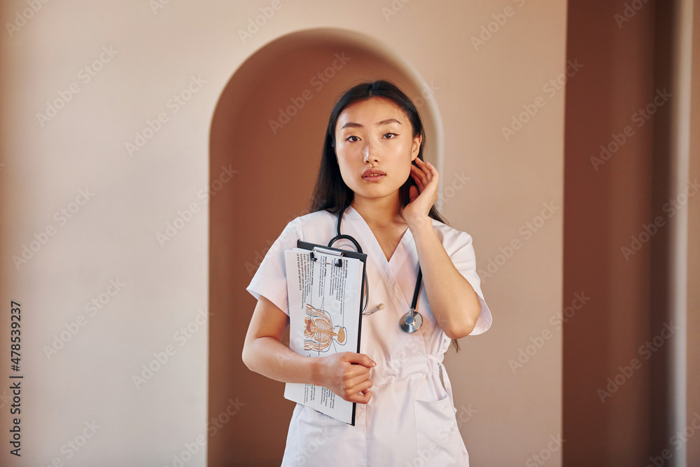 Wall mural Documents in hands. Young serious asian woman standing indoors