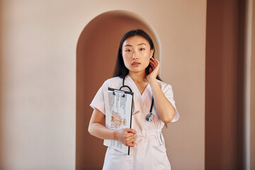 Documents in hands. Young serious asian woman standing indoors