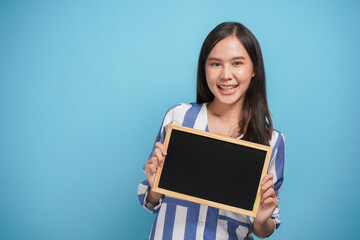 Obraz premium Pretty young woman holding and show empty blank black board for advertising banner and copy space on colorful background