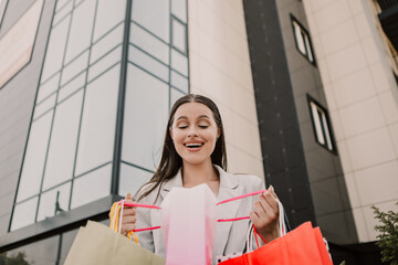 Surprised lady open and look into bags shopper woman dressed plaid blazer carrying enjoying new clothes packs things after shopping buyings sales black friday concept