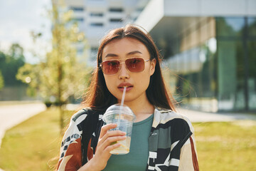 With fresh drink. Young asian woman is outdoors at daytime