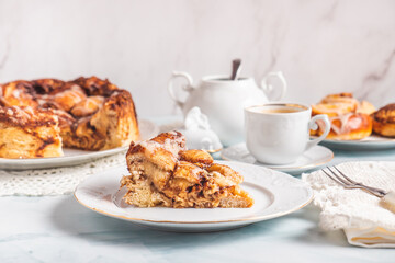 Portion of homemade cinnamon rolls on a white plate on a white table with coffee and pastry buns...