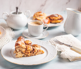 Portion of homemade cinnamon rolls on a white plate on a white table with coffee and pastry buns for breakfast. Traditional Swedish and Danish recipe.