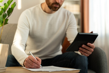 Pensive concentrated bearded man sitting at the table and studying paper bills while counting