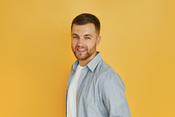 Young man in casual clothes standing indoors in the studio against orange background