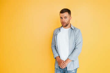 Shy young man in casual clothes standing indoors in the studio