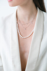 Trending silver necklace with pearls on a beautiful young girl in a white fashionable jacket. Beauty and fashion 

