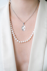 Trending silver necklace with pearls on a beautiful young girl in a white fashionable jacket. Beauty and fashion 
