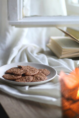 Lit candle, open books, reading glasses and plate of gluten free cookies on the table. Hygge at home. Selective focus.