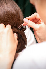 Fototapeta premium A hairdresser is making the hairstyle of a young brunette woman in a hair salon, close up