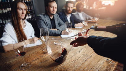 Sommelier and bartender training. Close-up of man pouring red wine from bottle into decanter