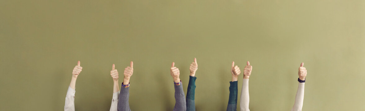 Team of satisfied people giving thumbs up. Group of four anonymous Caucasian males and females raising hands and doing like gesture. Banner background, studio shot of human hands showing thumb up sign