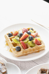 Belgian waffles with fruits berries and honey maple syrup set on white cafe table.