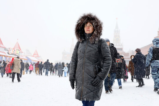 Blizzard in winter Moscow, woman on Red square in crowd of people walking on background of Kremlin and St Basils Cathedral during snowfall