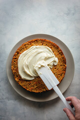 media tarta de zanahoria siendo untada con queso crema, sobre un fondo gris claro, con espacio en blanco