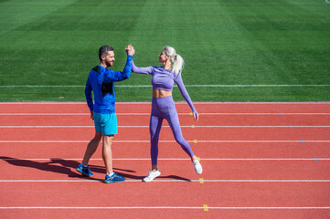 Obraz premium sport couple celebrate team win. fitness partners. athletic man and sexy woman compete in armwrestling. male and female coach on stadium running track arena. healthy lifestyle