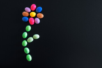 Sweets and confetti arranged in the shape of a flower. Confetti of different color and taste. Dark...