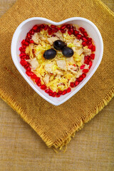 Puff salad with chicken breast, garnished with pomegranate and olives in a salad bowl on a napkin.
