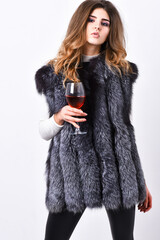 Fashion model long hair fur coat or vest hold wineglass. Girl enjoy luxury lifestyle attributes. Woman drink wine wear luxury fur clothing. Luxury lifestyle concept. Fashionable lady likes luxury