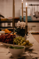 Festive table with burning candles gold candlestick. Red and green grapes in a white bowl.